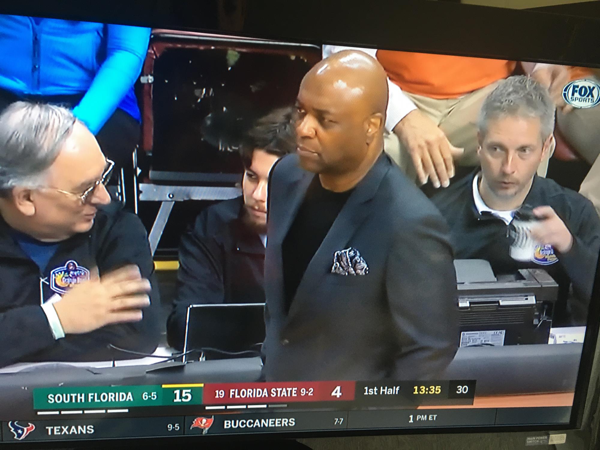 Dodson at the table (behind coach Leonard Hamilton) working at the 2019 Orange Bowl Classic Basketball Tournament. Dodson says, “Like we always preach, when a coach or an inbound pass is in front of you ‘look busy, you are on TV’. I obviously didn't listen to that advice (mid-coffee drink).”